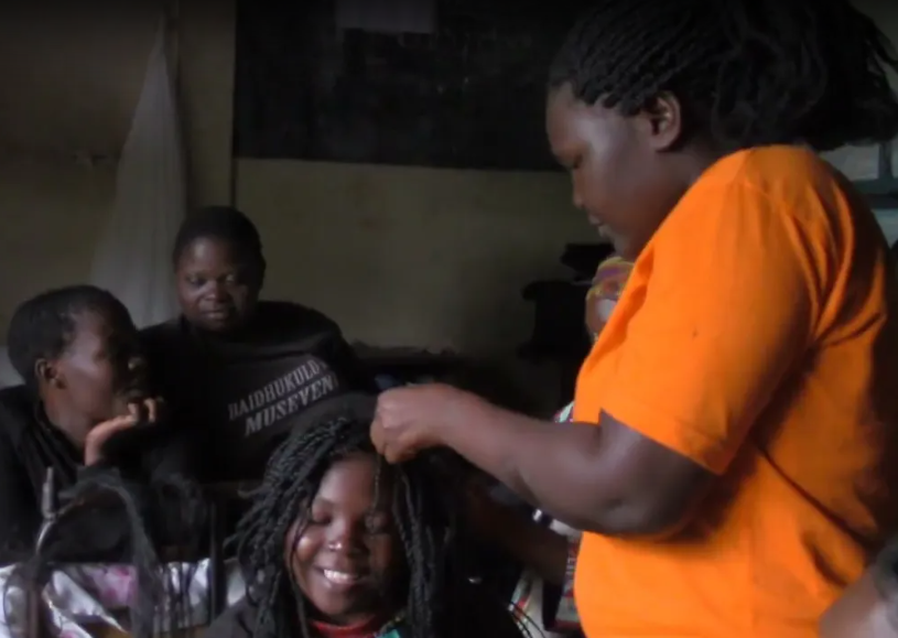 Gorret Namwanje, a young Ugandan woman, braids a girl's hair.