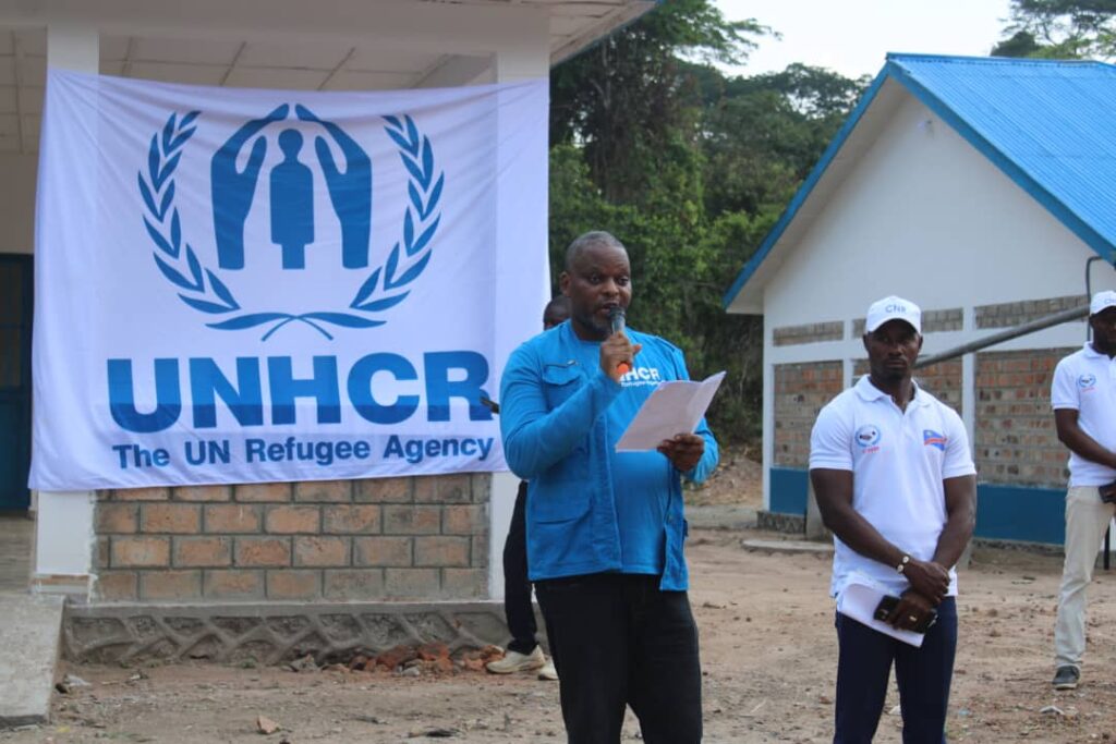 Former UNHCR senior field assistant John Luboya Kalonji.speaks outside with a microphone. A UNHCR banner is behind him.