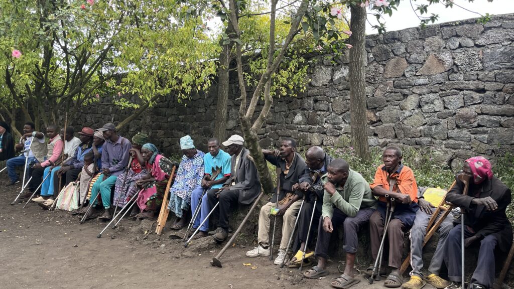 People with disabilities sit along a wall outside. They are participating in Youth4Climate's clean cooking program in Goma.