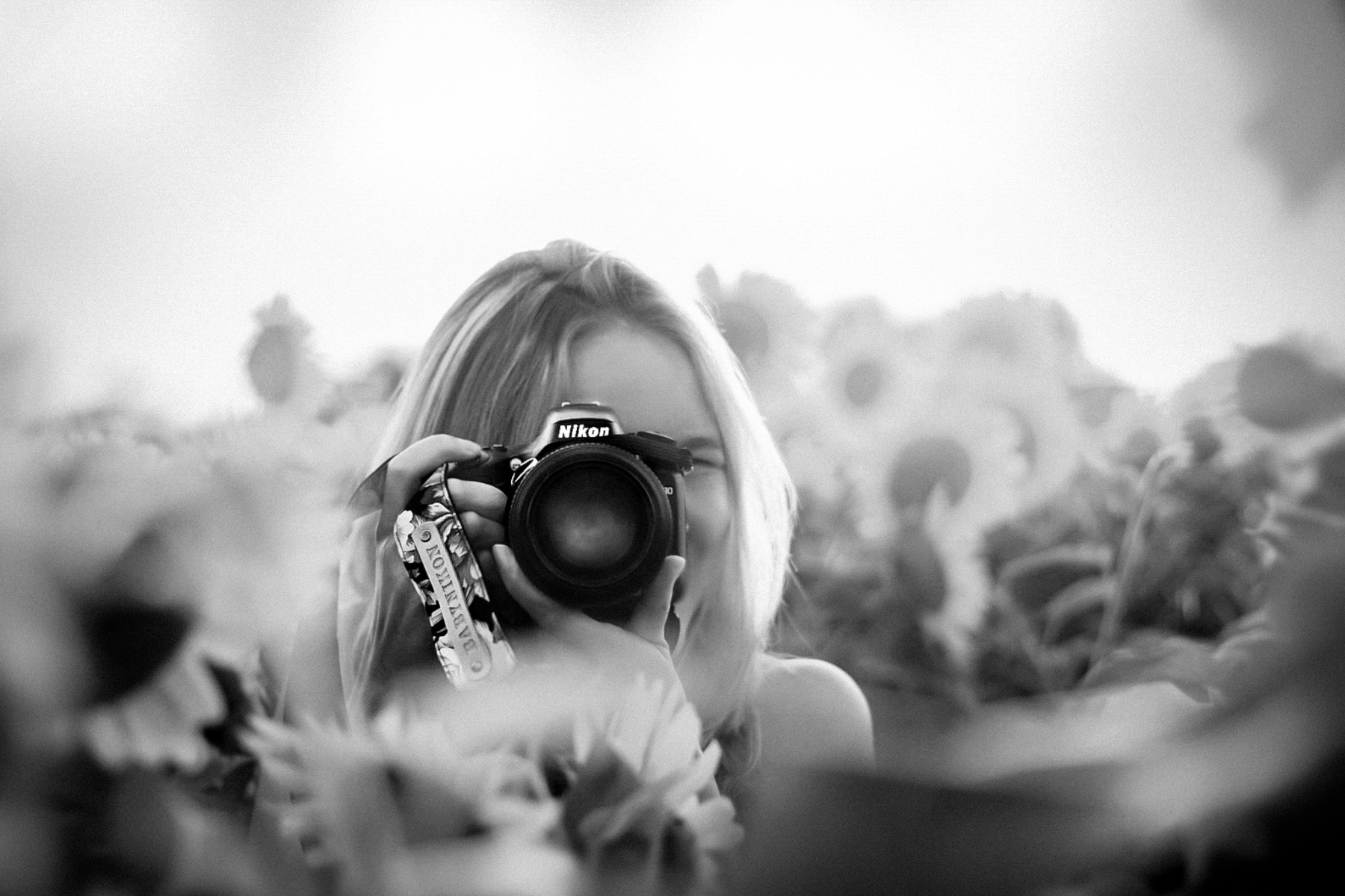 A black-and-white photo of Marian holding a camera to her eye in a field of sunflowers.
