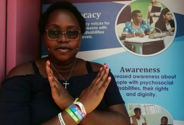 Esther Suubi poses for the camera in front of a Triumph Mental Health banner.