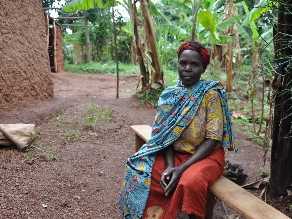 Angelique Tuyishimire's mother sits on a wooden bench outside.
