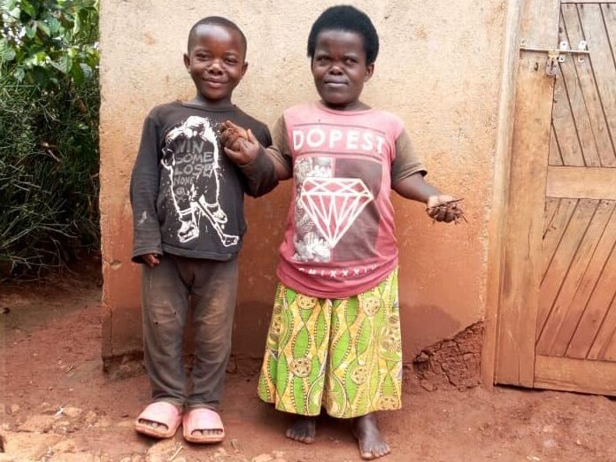 Claudine Bihoyiki and her son stand outside in front of a clay wall. 