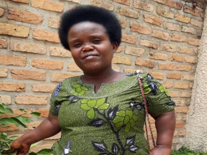 Veneranda Nibagwire stands in front of a brick wall.