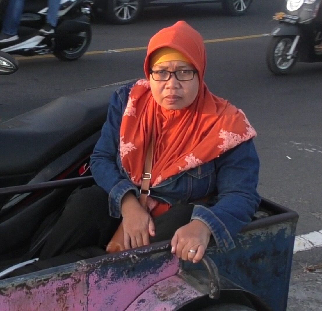 Sri Sukarni sits in a motorbike sidecar, looking at the camera.