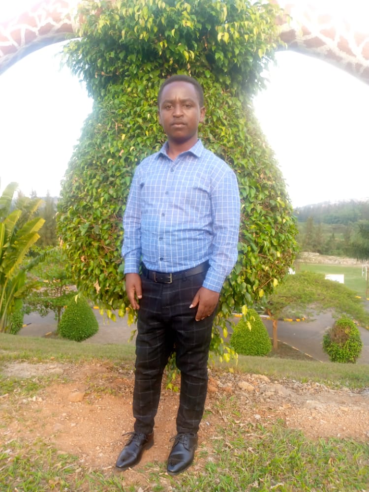 Manasseh Nzanira stands in front of a tree, looking at the camera. 