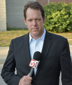 MIke Beaudet holds a microphone and looks at the camera.