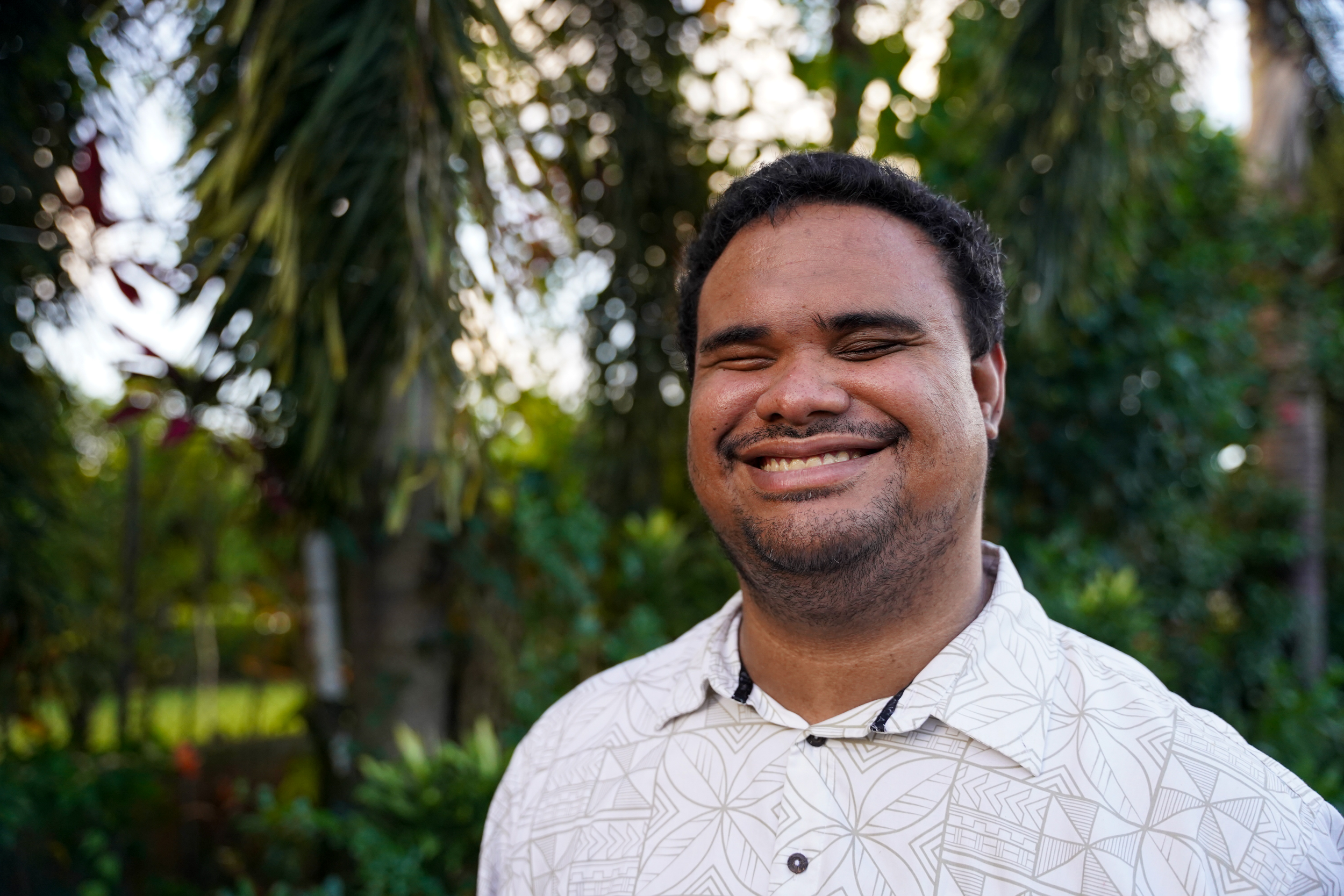 Ari Hazelman smiles broadly at the camera. He is standing outside with trees behind him.