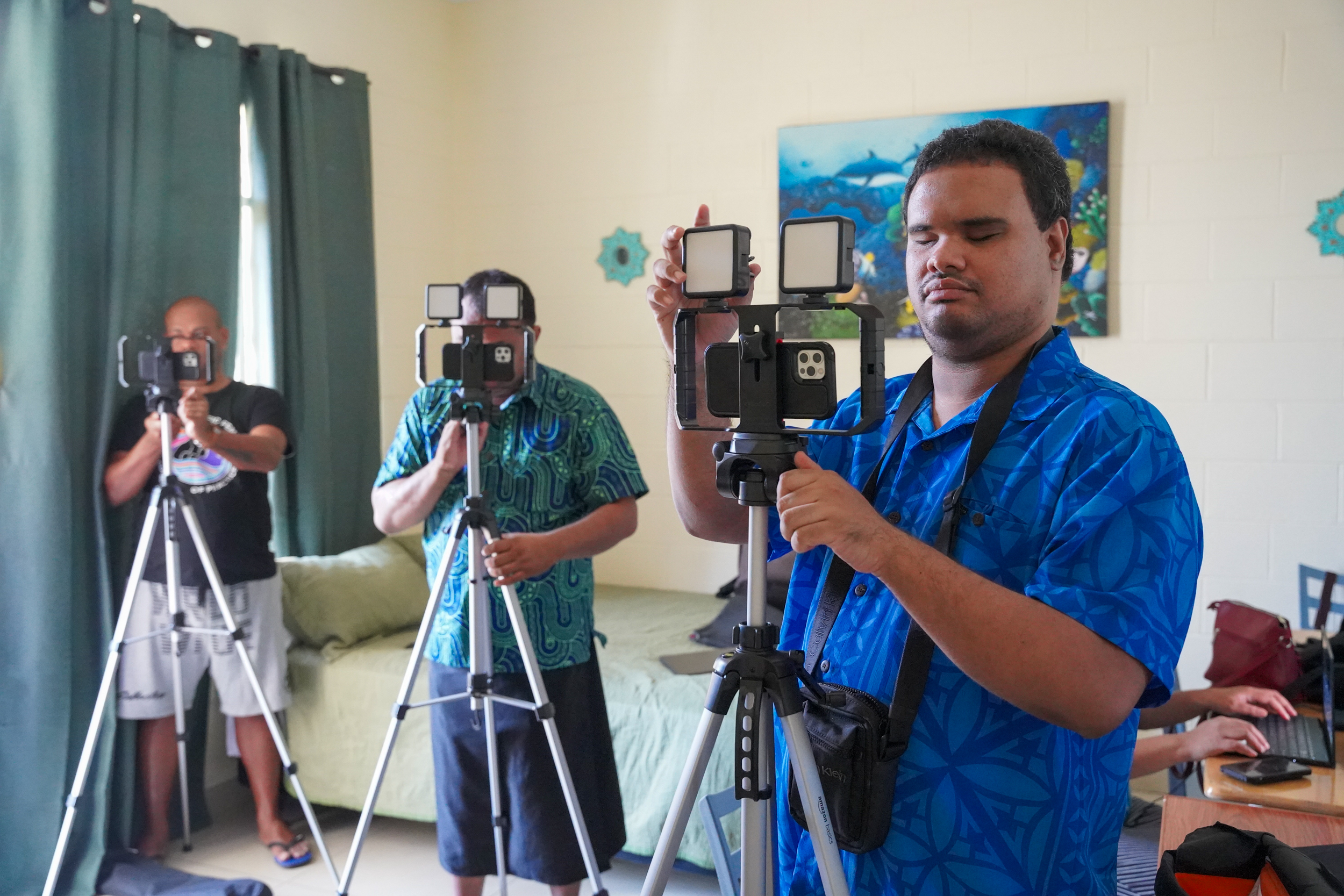 Three fellows with the Disability Justice Project stand behind their cameras in a room. One is blind and one is low vision.