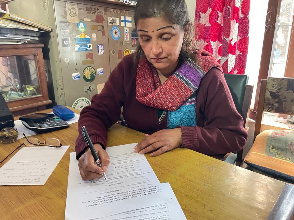 Satya Devi Wagle sits at her desk, signing papers.