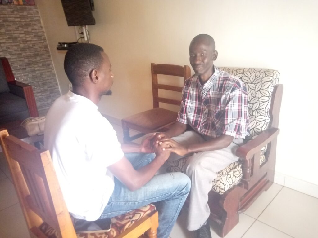 Jean Marie Furaha, a DeafBlind advisor at the Rwanda Organization of Persons with Deaf Blindness, uses tactile sign language to communicate with a Rwandan man sitting across from him.