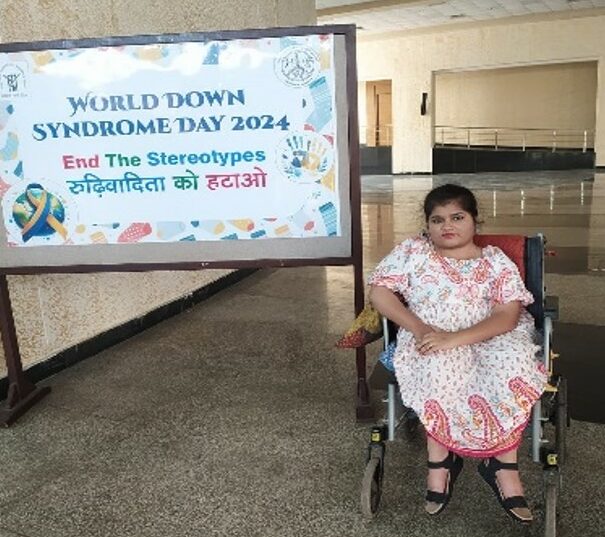 Priya Srivastava sits in her wheelchair in front of a sign that says, "World Down Syndrome Day. End the stereotypes."