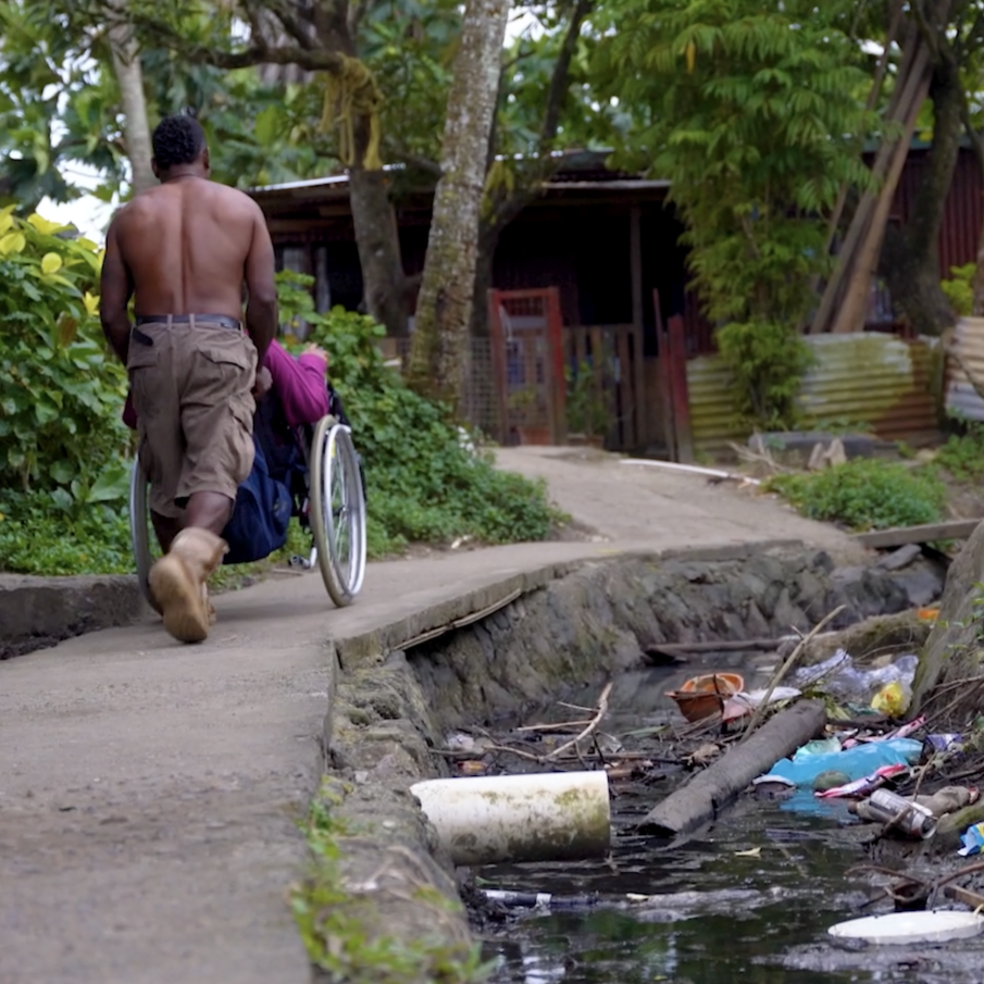 A man pushes a woman in a wheelchair in an informal settlement in Fiji.