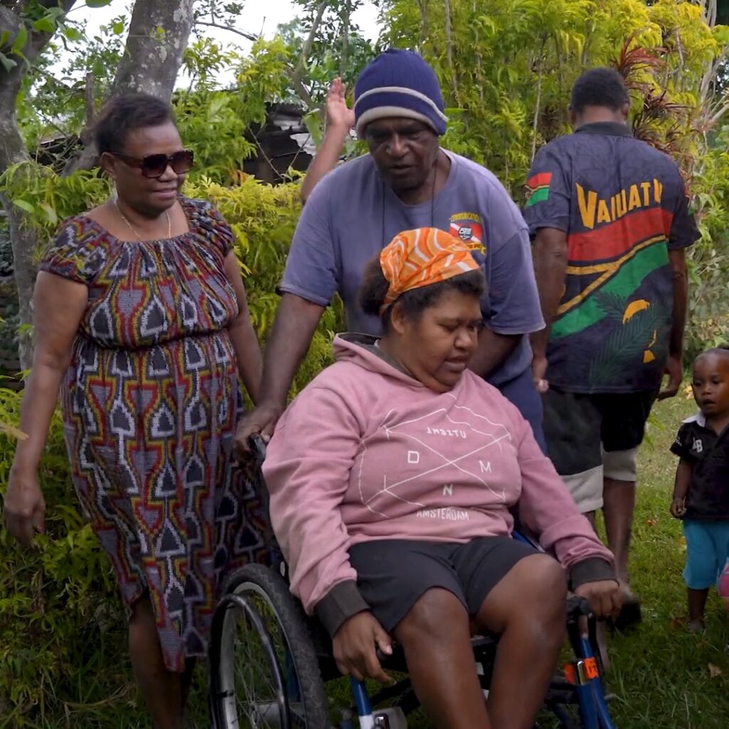 Two people push a woman in a wheelchair in Vanuatu.