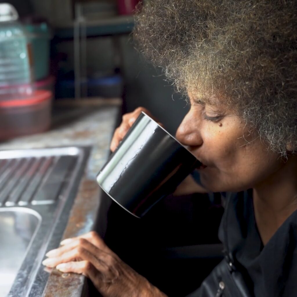 Mere Rodin, a Fijian woman, sips water from a cup.