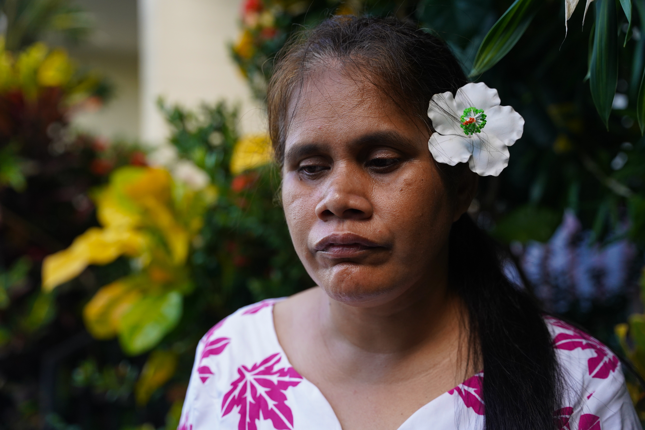 Faaolo Utumapu-Utailesolo stands in front of bushes and flowers with a white flower in her hair.