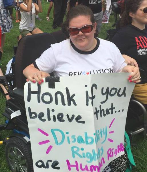 Emily Ladau holds a poster that says, "Honk if you believe disability rights are human rights."