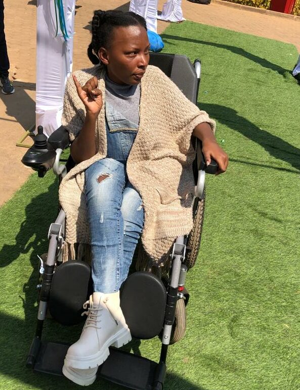 Marie Aime Dukuzem, a young Rwandan woman in a wheelchair, holds up her ink-stained pinky finger to show that she's voted.