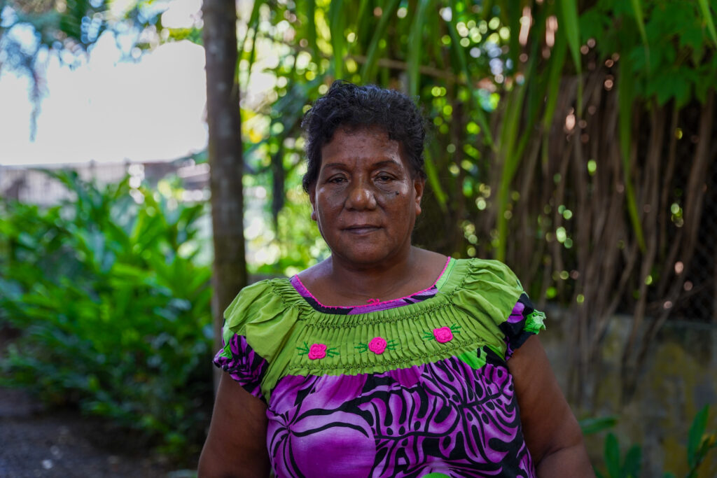 Rubi Nabetari, an I-Kiribati woman, stands in front of trees and looks into the camera.