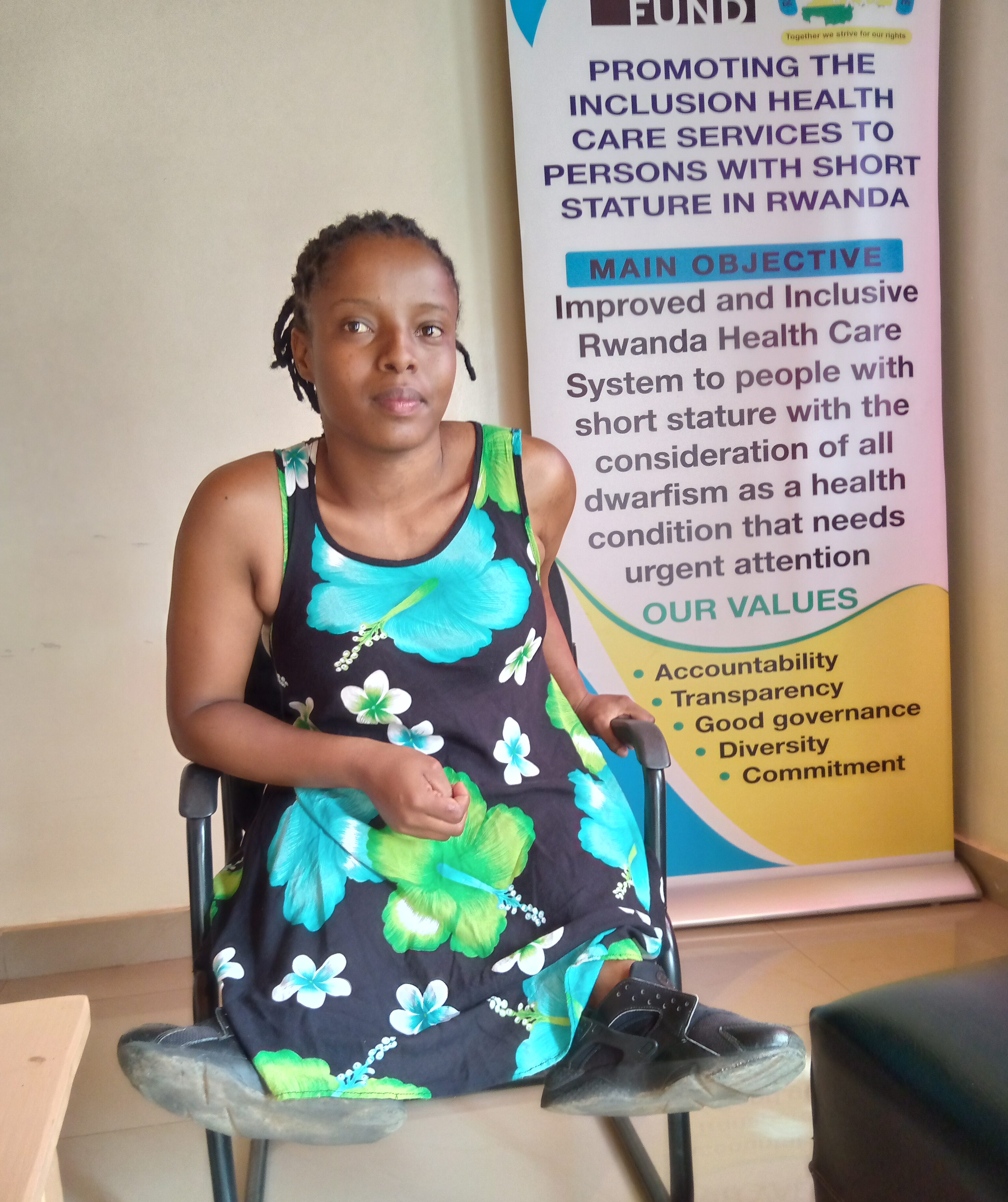 Alliance Ukwishaka, a young Rwandan woman, sits in a wheelchair in front of a banner about inclusive health services.