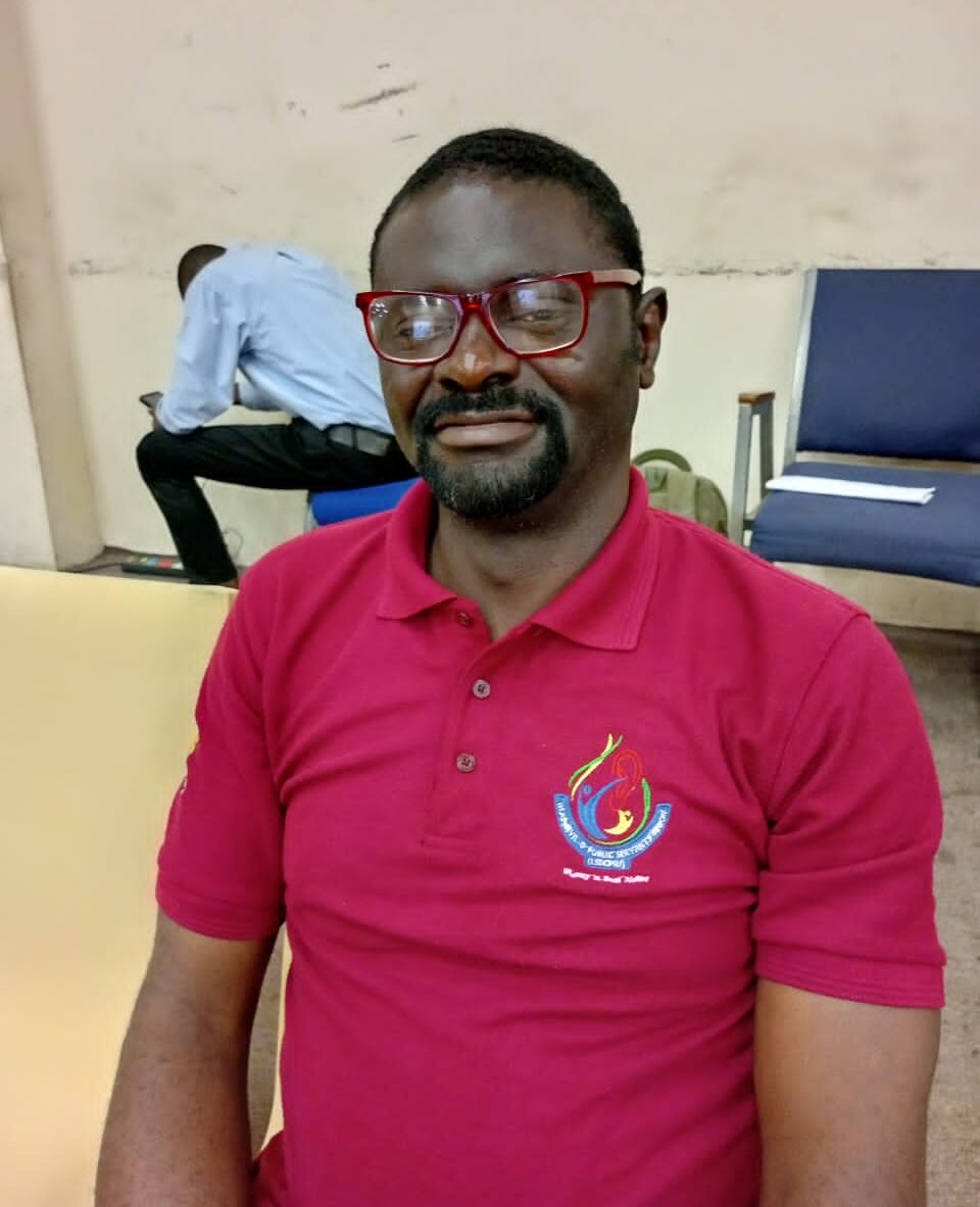 John Shodiya, a DeafBlind man, poses for a photo. He is wearing a red, short-sleeve polo shirt and red glasses.