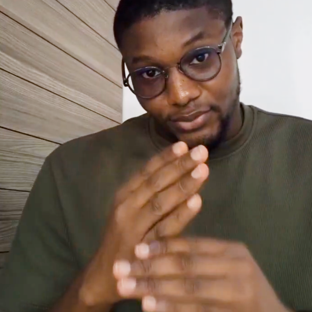 Douglas Izu, a Deaf Nigerian man, signs to the camera. An image of the nation of Nigeria is behind him.