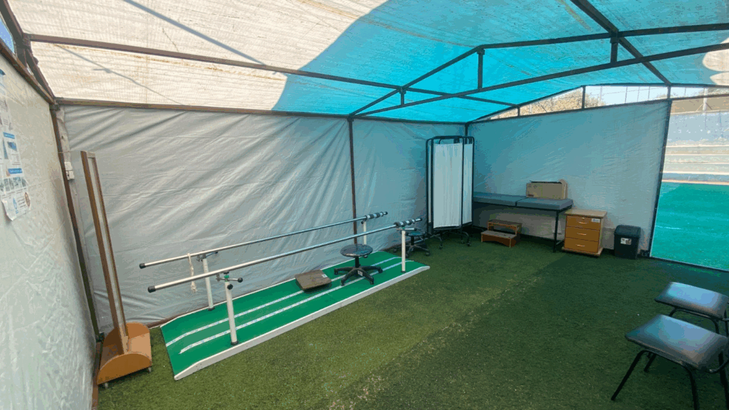 Inside a tented rehabilitation room with a blue tarp roof and artificial grass floor.