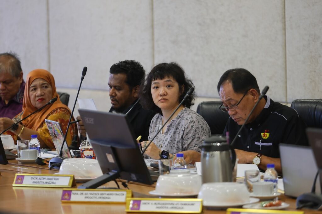 Beatrice Leong attends a Malaysia National Council for Persons with Disabilities meeting. She sits at a table, surrounded by other members.