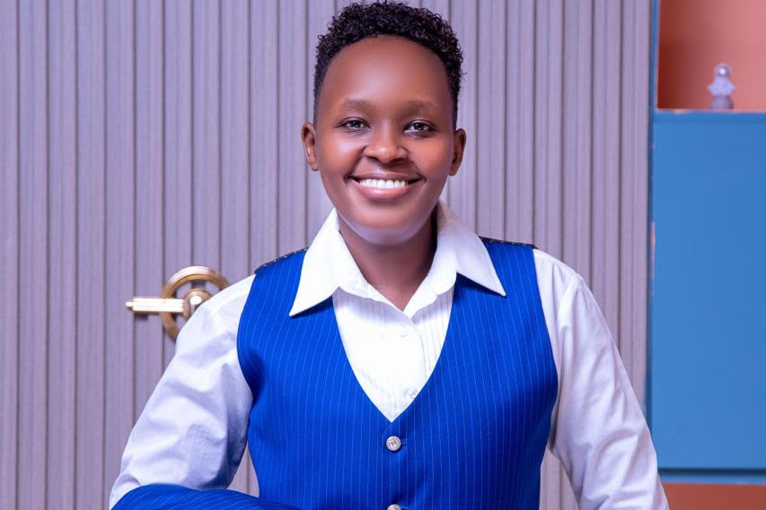 Wanjiku Mwangi smiles at the camera, wearing a blue pinstripe suit and white shirt and holding a matching jacket.