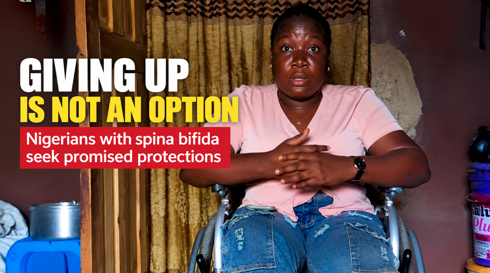 A woman wearing a light pink shirt and blue jeans sits in a wheelchair inside her home, facing the camera with her hands clasped. Large white and yellow text reads “Giving Up Is Not an Option.” A red banner below reads “Nigerians with spina bifida seek promised protections.”